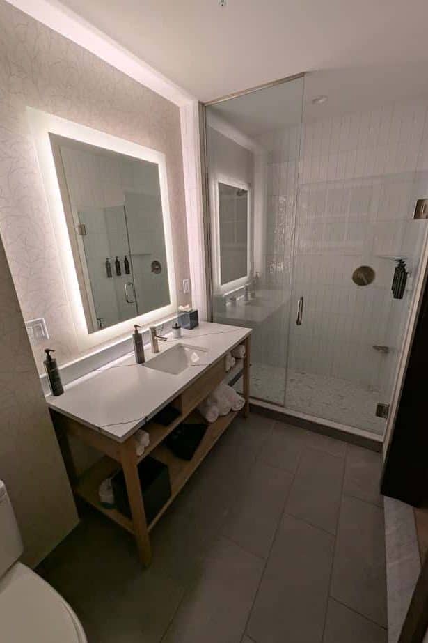 Modern bathroom with a spa-like ambiance featuring a backlit mirror, sink, wooden vanity, and glass shower enclosure—perfect for relaxing after a day at Skaneateles Fields Resort in the Finger Lakes.