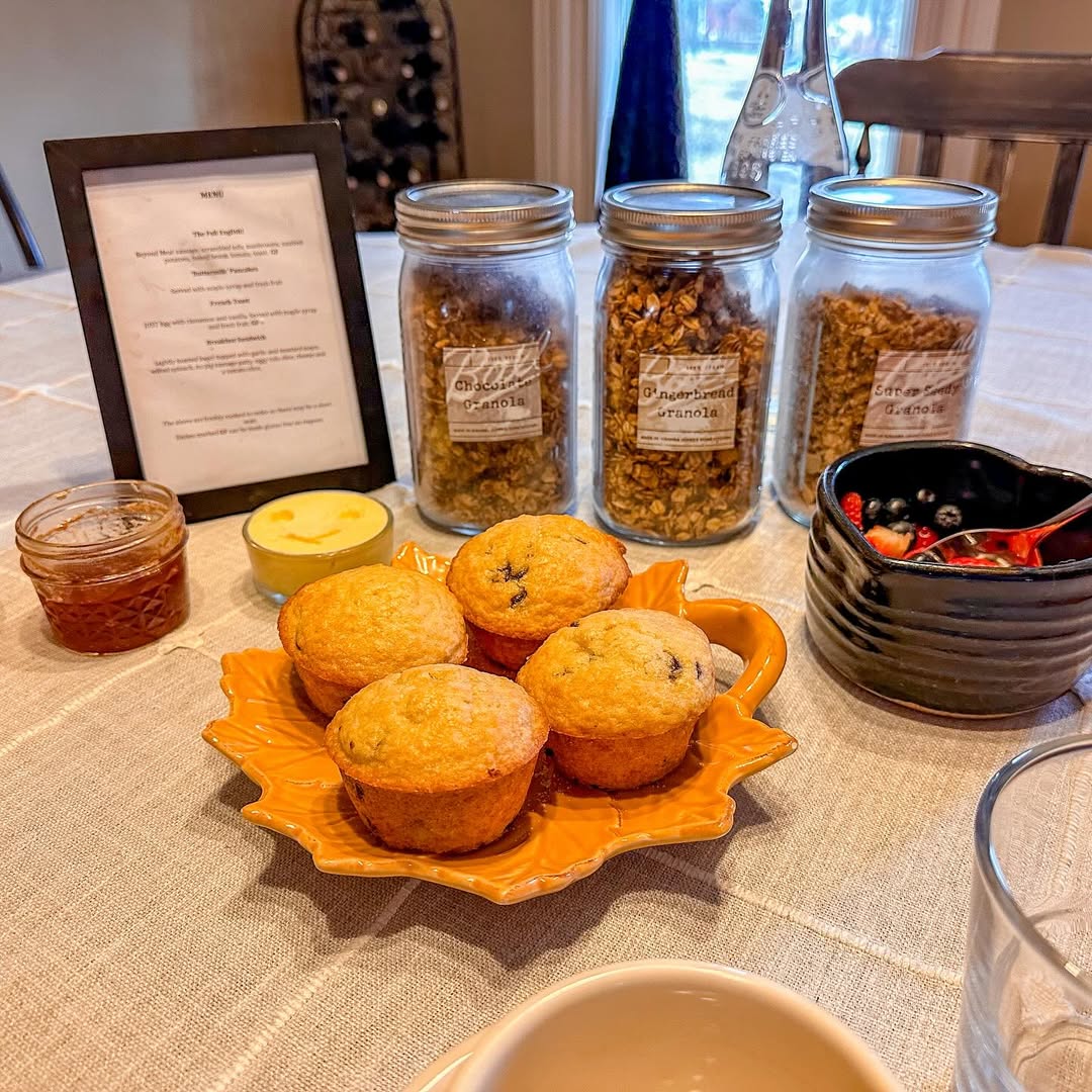 A table set with muffins, granola jars, jam, berries, and a framed menu on a light tablecloth evokes mornings at the best places to stay in Finger Lakes near wineries.