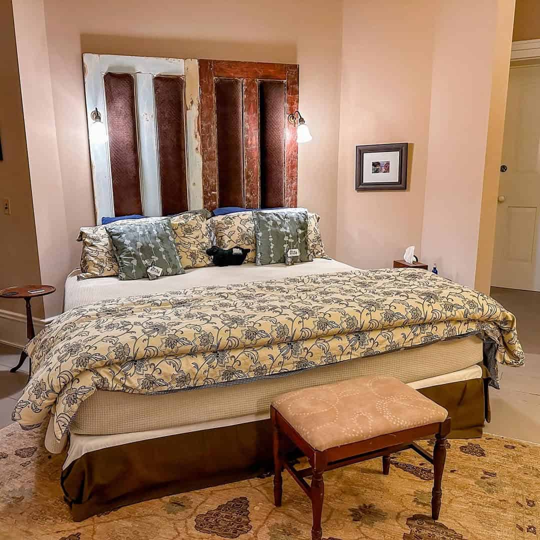 A cozy bedroom with a patterned bedspread, pillows, a rustic headboard, and a cushioned bench at the foot of the bed—one of the best places to stay in Finger Lakes near wineries.