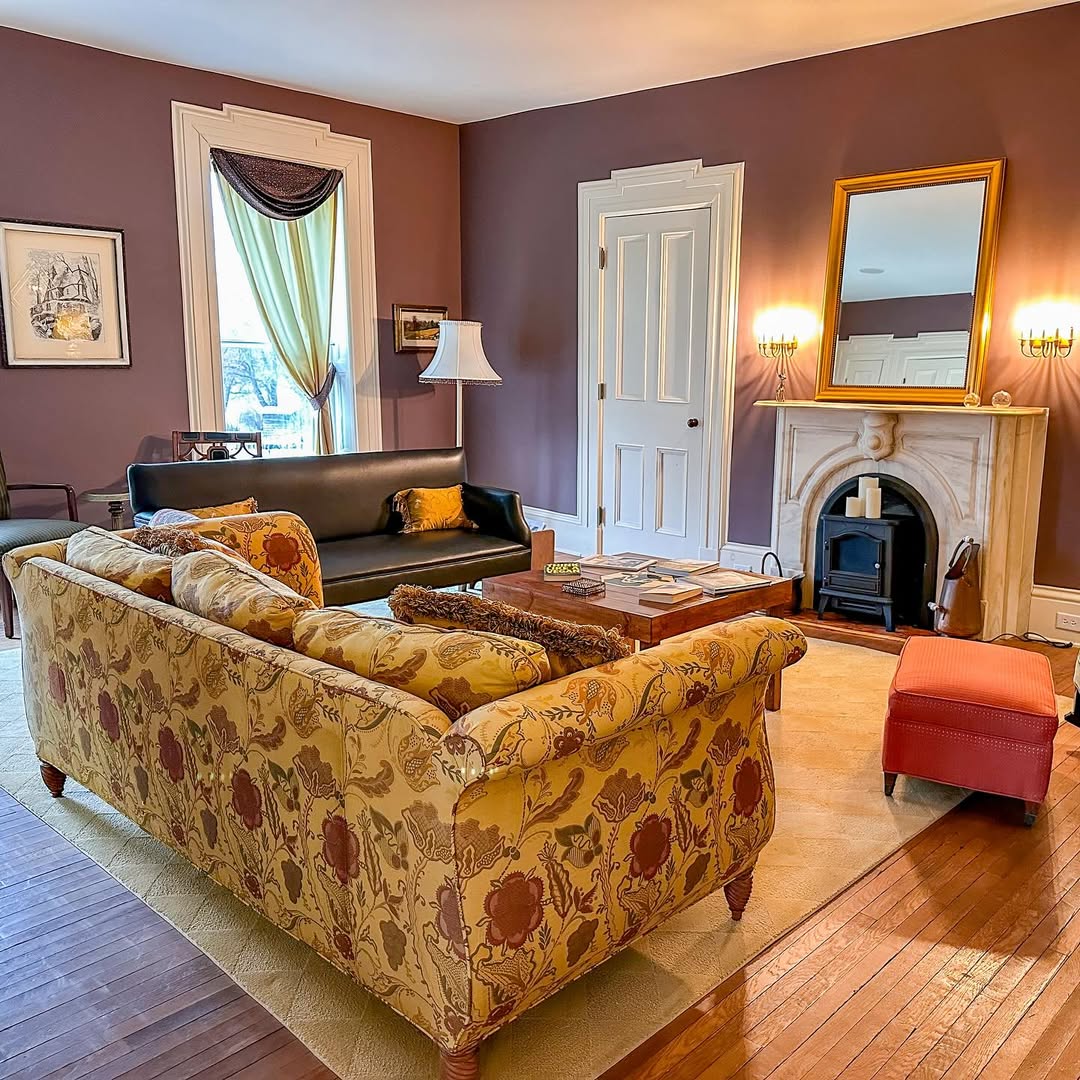 Elegant living room with floral sofa, fireplace, mirror, and large window with drapes—one of the Best Places to Stay in Finger Lakes Near Wineries.