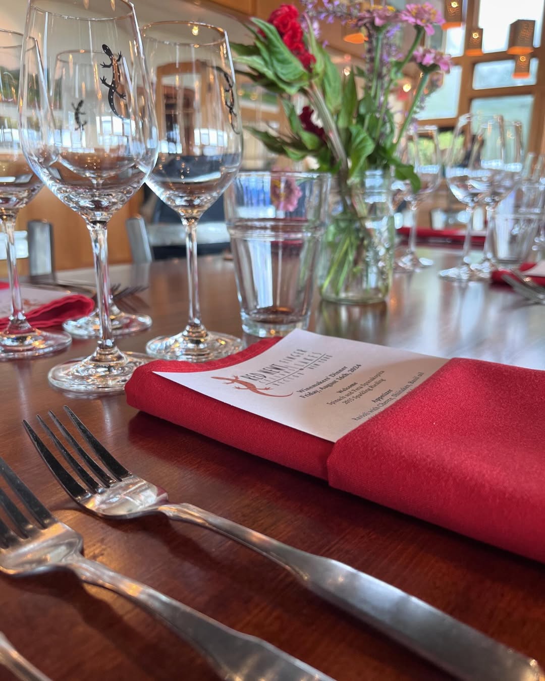 Close-up of a dining table set with wine glasses, red napkins, menus, and a vase of flowers at one of the elegant Finger Lakes restaurants.