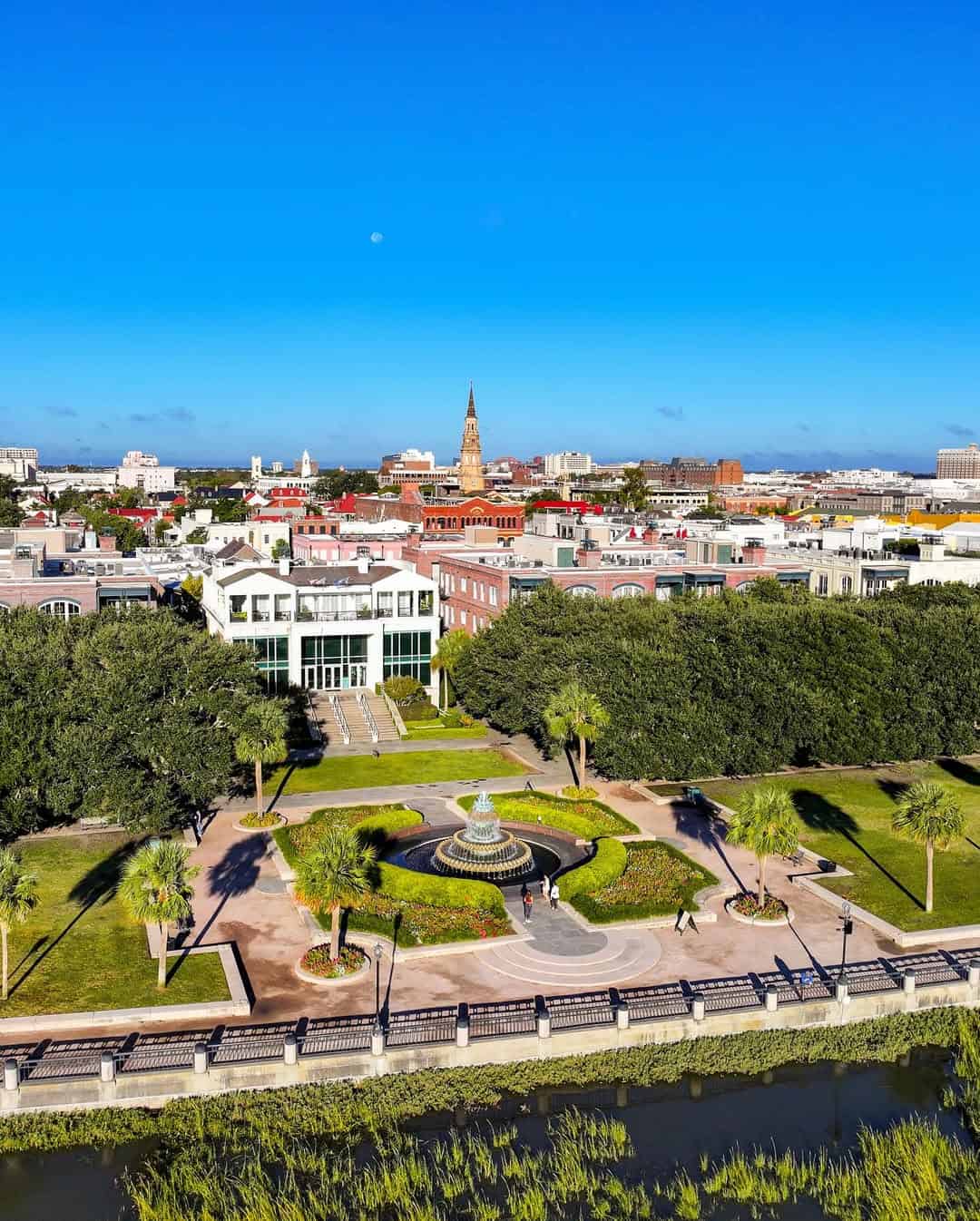Aerial view of a city park with a fountain, trees, and buildings under a bright blue sky—one of the top things to do in Charleston with kids.