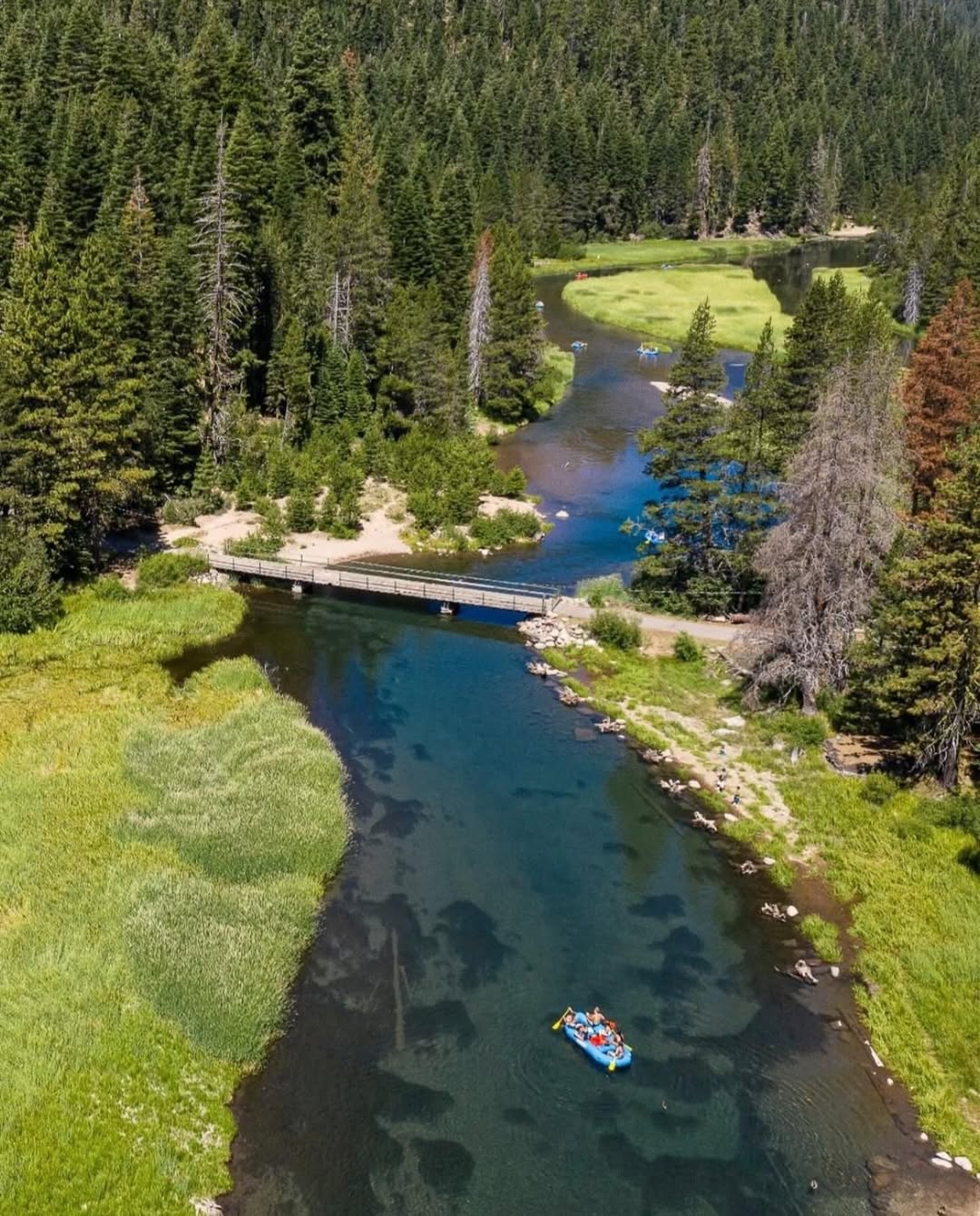 Aerial view of a river with people rafting, surrounded by dense forest and a small wooden bridge—perfect inspiration for a family vacation to Lake Tahoe.