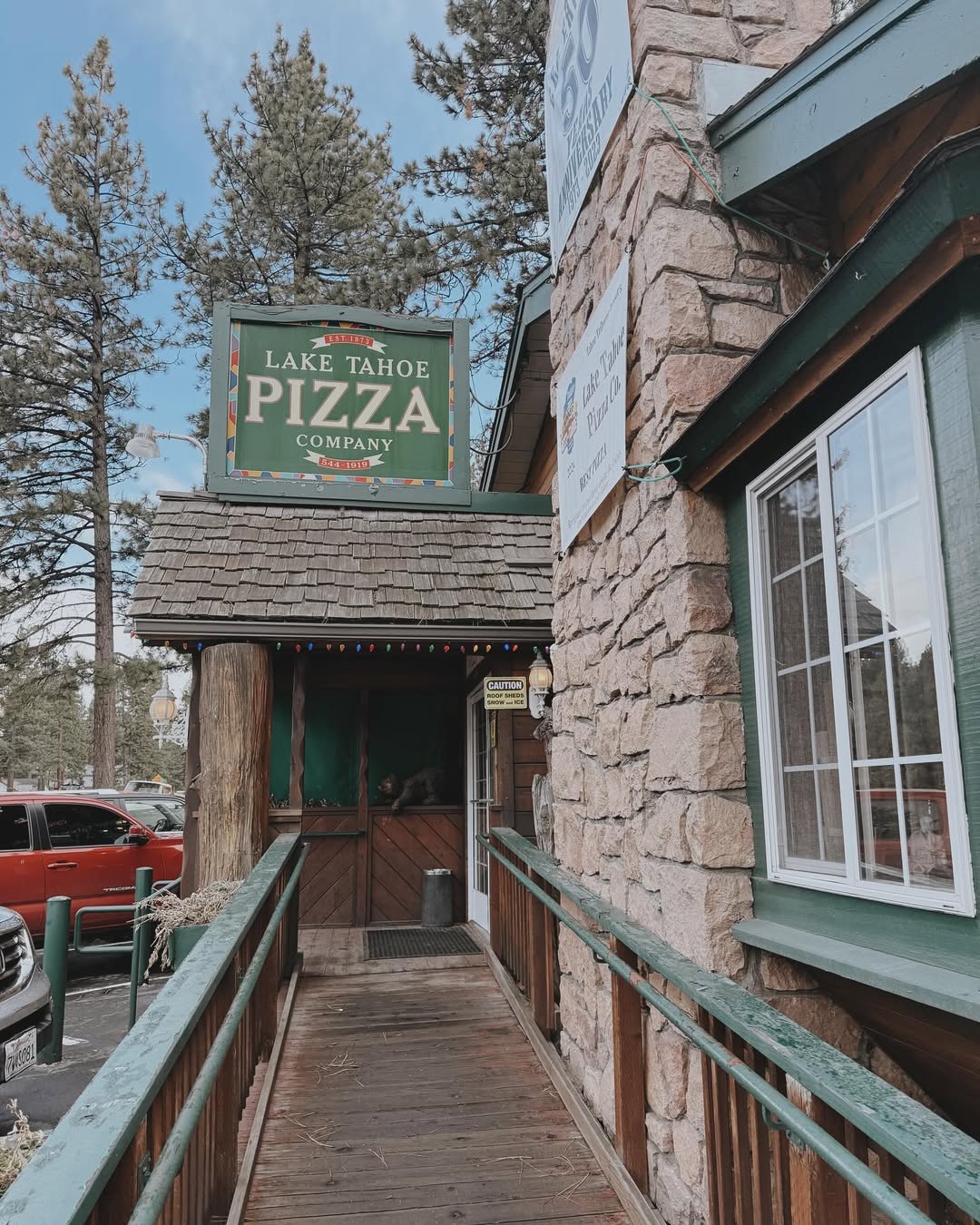 Wooden ramp leading to the entrance of Lake Tahoe Pizza Company, with trees and cars visible in the background—perfect for a family vacation to Lake Tahoe.