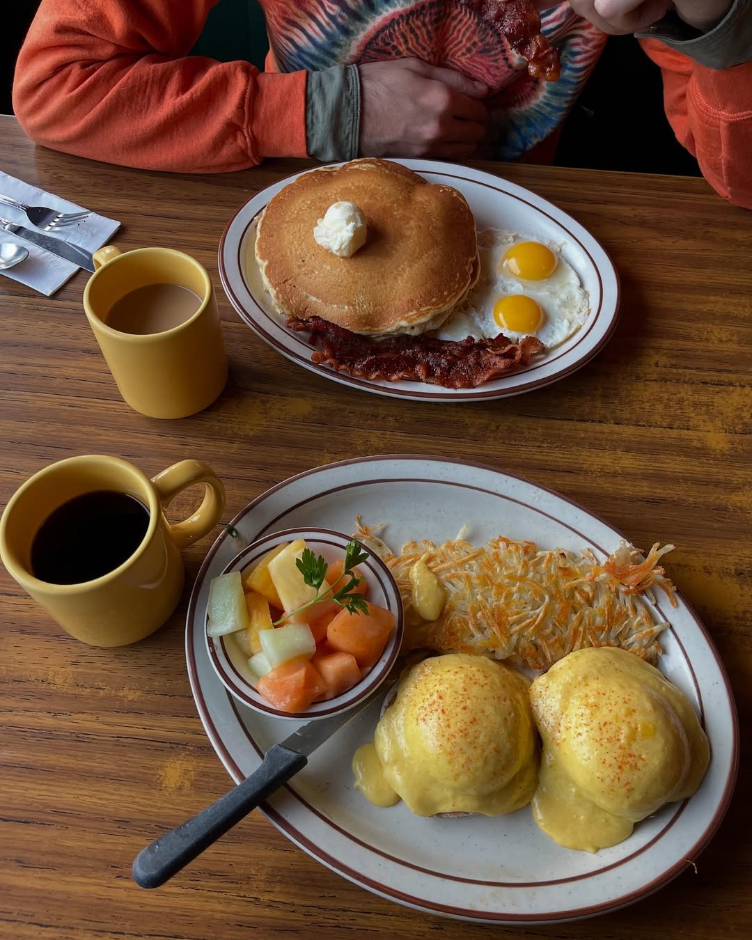 Two plates of breakfast food—one with pancakes, eggs, and bacon, the other with eggs Benedict, fruit, and hashbrowns—ready to kick off a perfect family vacation to Lake Tahoe.