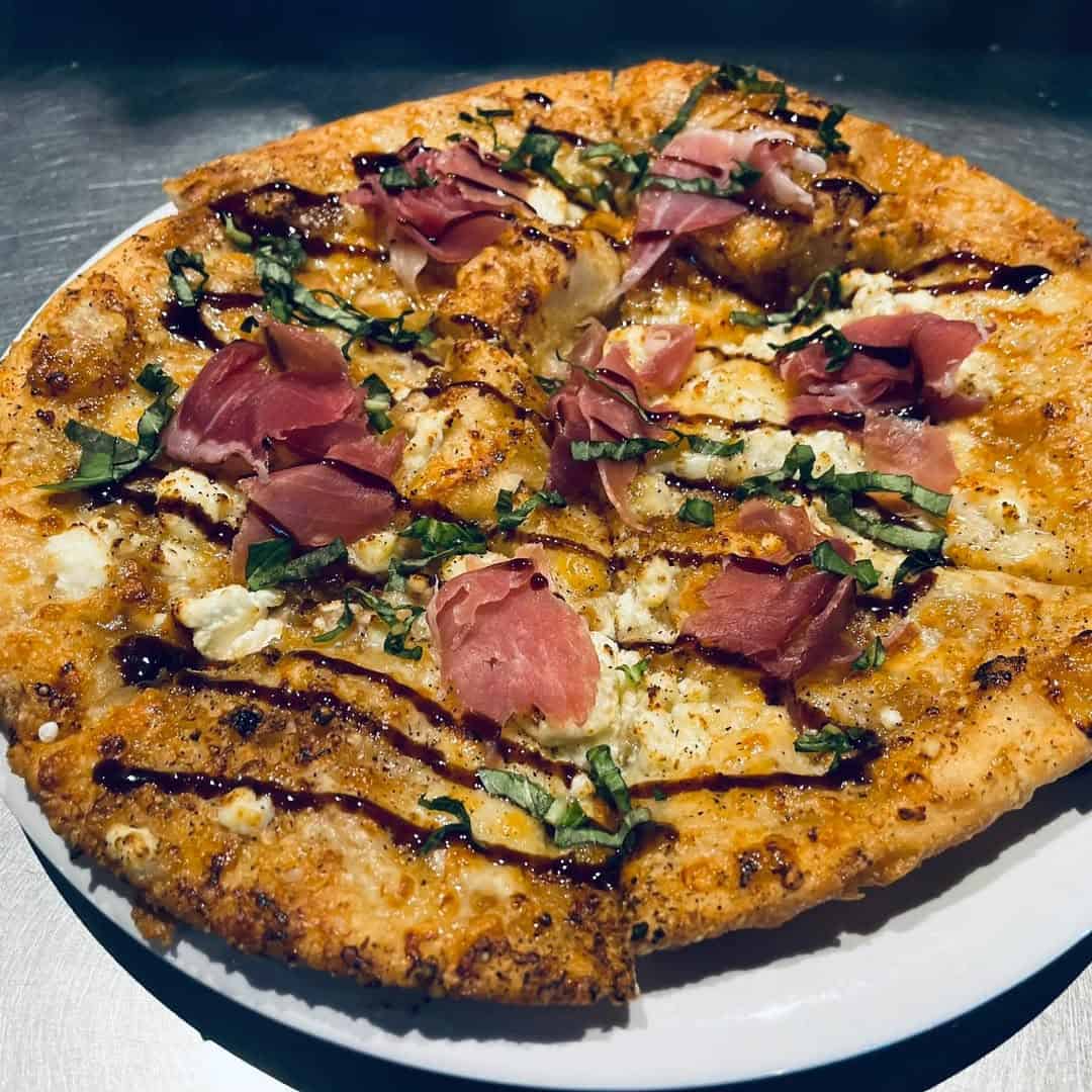 Pizza with prosciutto, cheese, fresh basil, and balsamic glaze on a white plate&mdash;perfect for pairing at Finger Lakes wineries with restaurants.