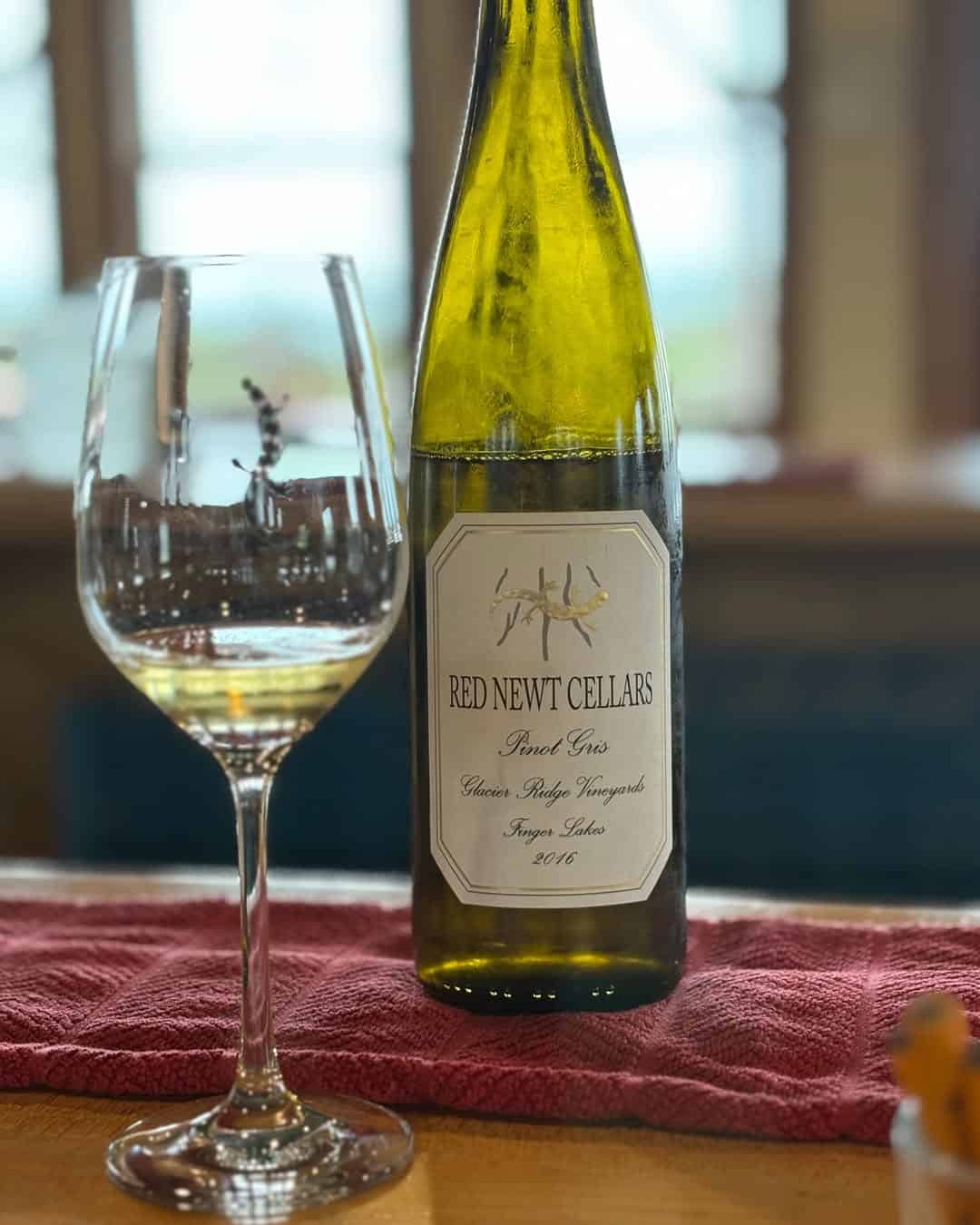 A glass of white wine and a Red Newt Cellars wine bottle on a red cloth, indoors&mdash;perfect for those seeking top Finger Lakes wineries with restaurants.