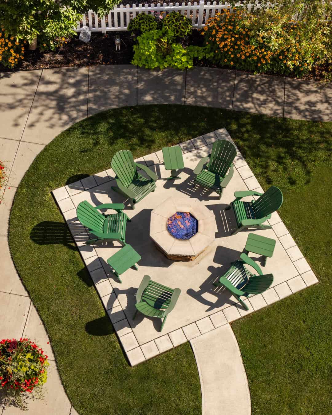 Aerial view of green chairs in a circle around a fire pit on a patio, with grass and flowers nearby—one of the Best Places to Stay in Finger Lakes Near Wineries.