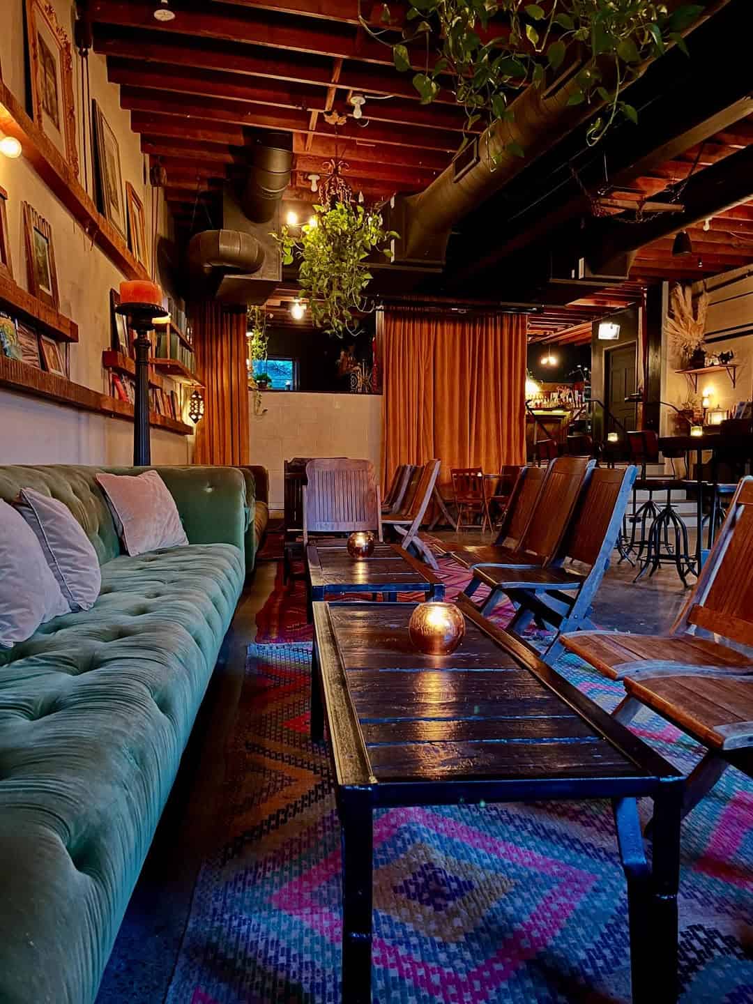 Cozy lounge with a green velvet sofa, wooden chairs, candles, and warm lighting under exposed beams—one of the best places to stay in Finger Lakes near wineries.