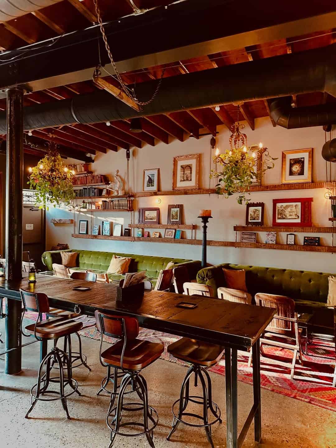 Cozy cafe with vintage decor, a green velvet sofa, framed art, hanging plants, and wooden tables—one of the best places to stay in Finger Lakes near wineries for a relaxing retreat.