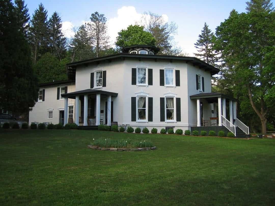 Large white house with green shutters, surrounded by trees and a well-kept lawn on a sunny day—one of the best places to stay in Finger Lakes near wineries.