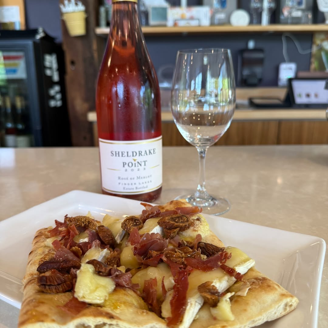 A glass and bottle of ros&eacute; wine from one of the Finger Lakes wineries with restaurants sits beside flatbread topped with figs, prosciutto, and cheese on a white plate.