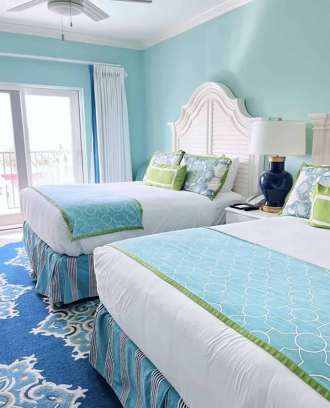 Bright bedroom with two double beds, blue and green bedding, patterned rug, and natural light from glass doors—perfect for families exploring things to do in Charleston with kids.