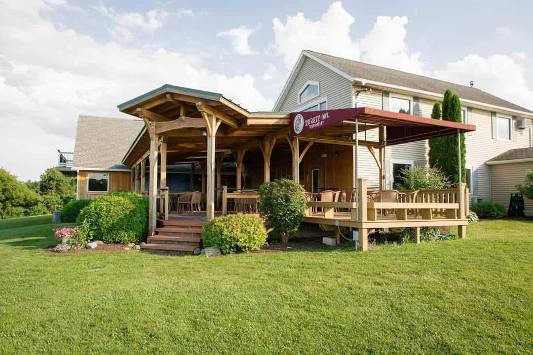 Wooden deck with tables and chairs attached to a house, surrounded by green lawn and shrubs on a sunny day&mdash;perfect for enjoying meals like those at Finger Lakes wineries with restaurants.