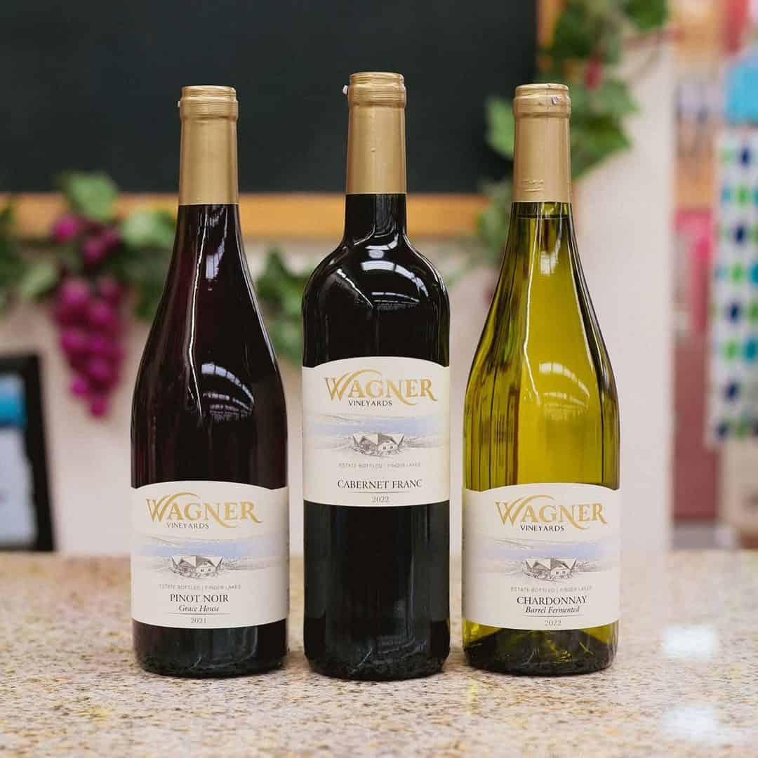 Three Wagner Vineyards wine bottles&mdash;Pinot Noir, Cabernet Franc, and Chardonnay&mdash;on a granite countertop, showcasing one of the premier Finger Lakes wineries with restaurants.