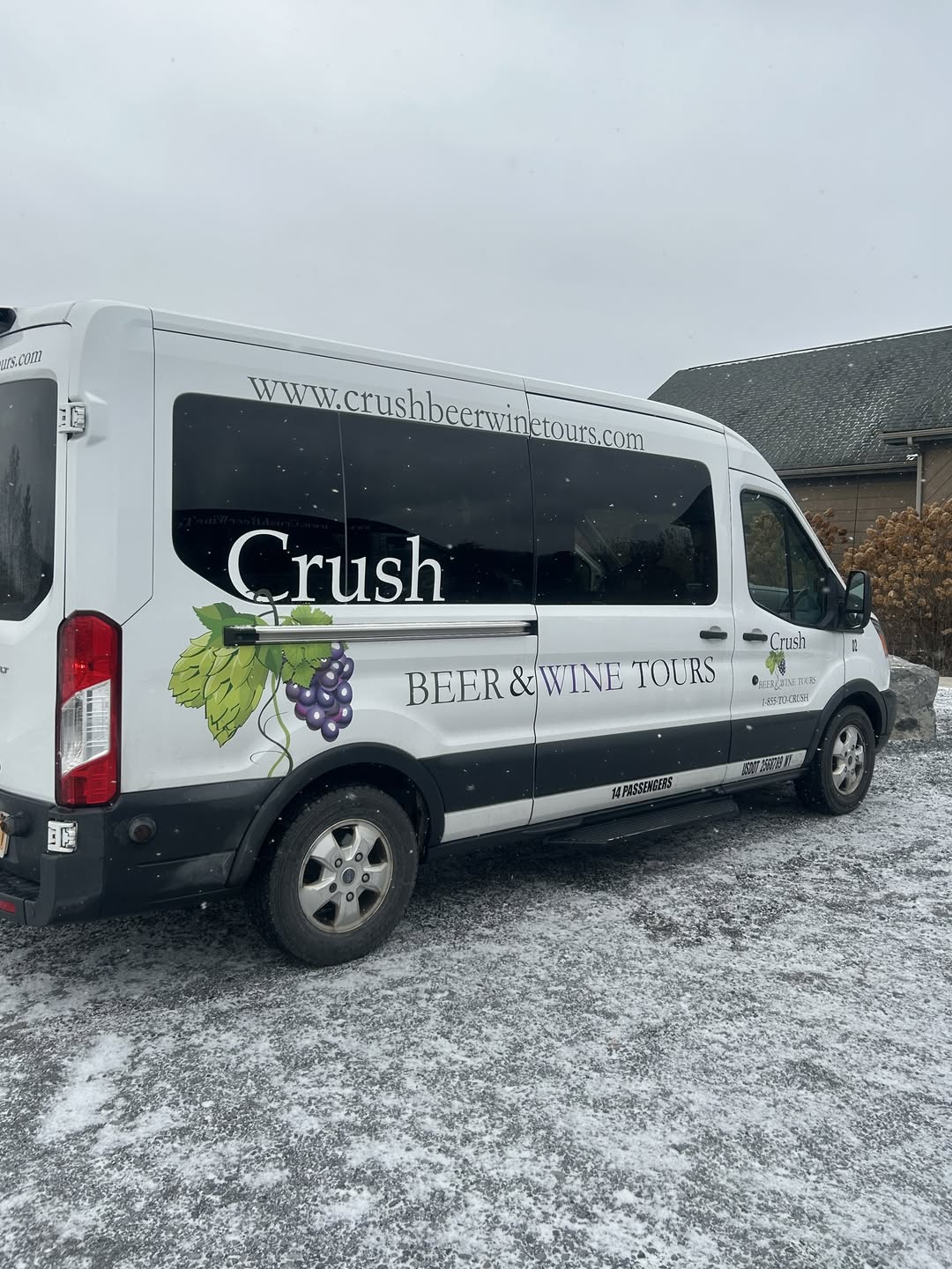 A white van with "Crush Beer & Wine Tours" and grape graphics, promoting Finger Lakes Wine Tours, is parked on snowy ground near a building.