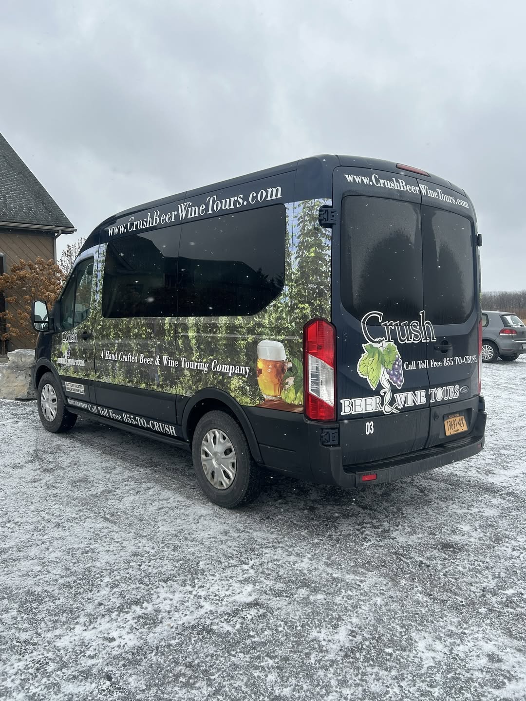 A black Crush Beer & Wine Tours van is parked on a snowy surface near a building, ready to embark on Finger Lakes Wine Tours.