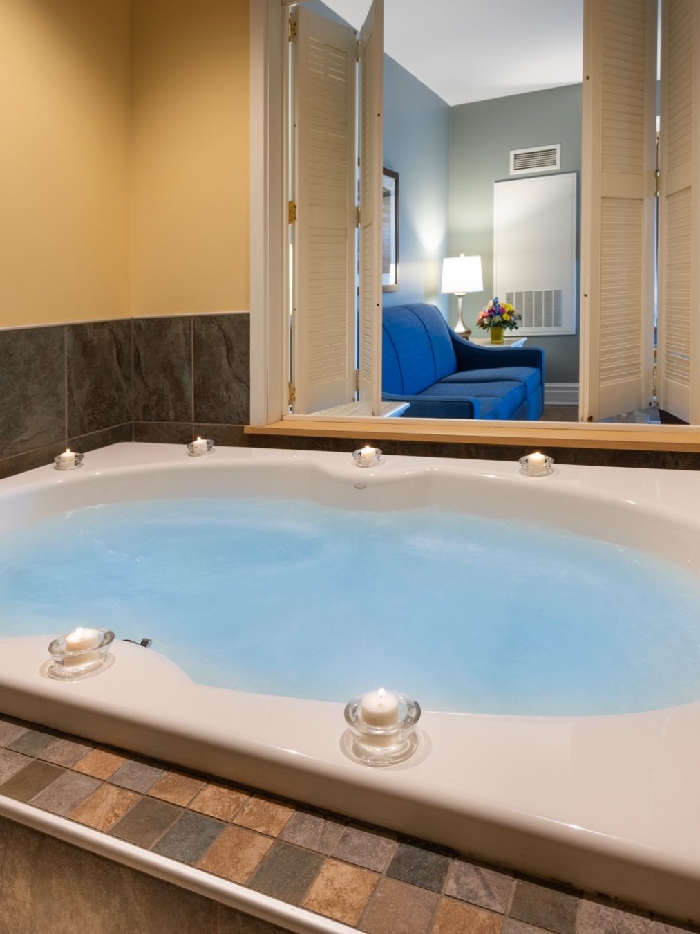 A white jacuzzi tub in a tiled room opens to a living area with a blue sofa and flowers—one of the Best Places to Stay in Finger Lakes Near Wineries for relaxation and scenic charm.