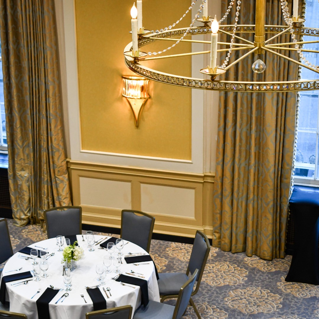 Elegant dining table set for six under a large chandelier in a formal, carpeted banquet room—perfect for family gatherings and discovering unique things to do in Charleston with kids.