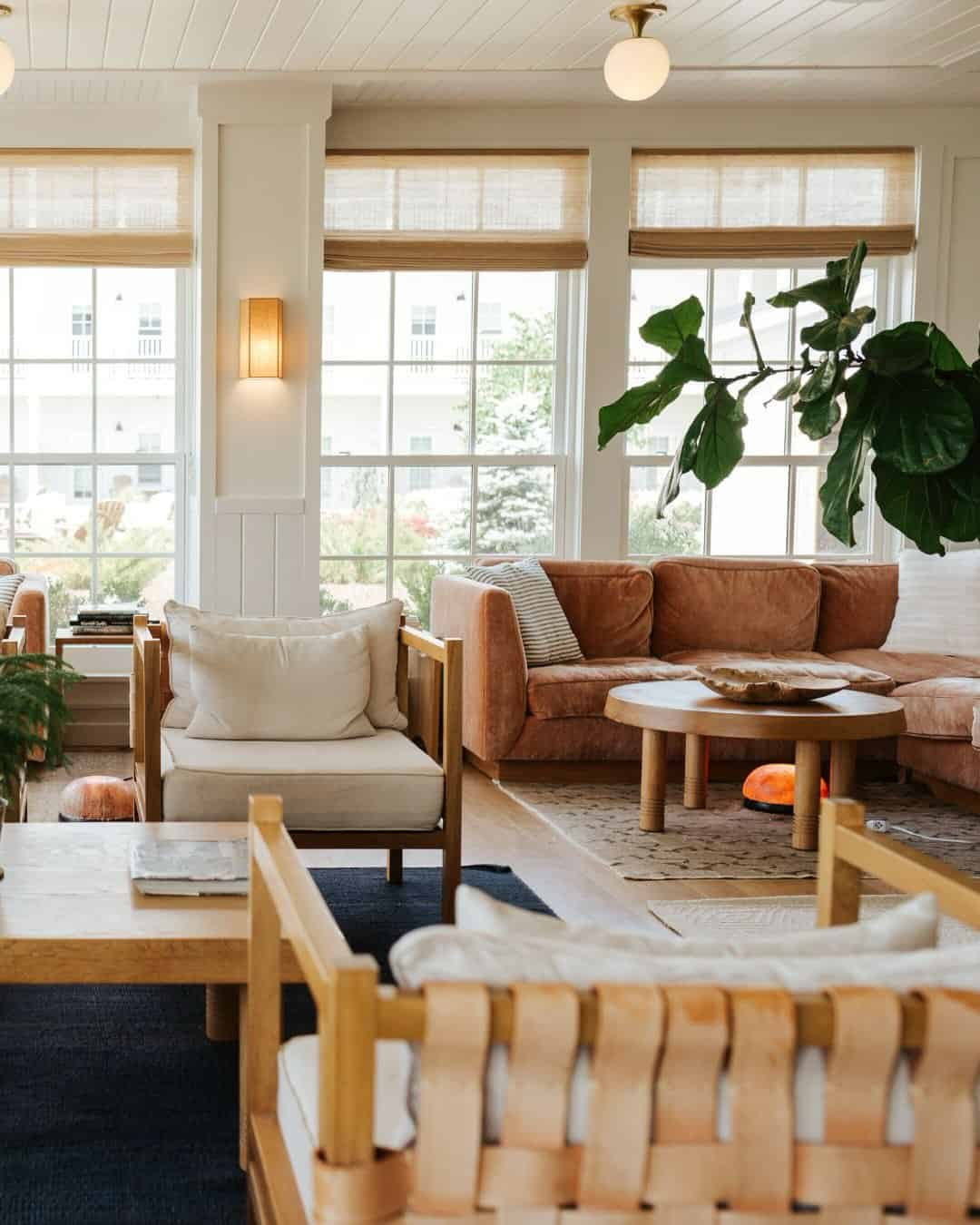 Bright living room with large windows, tan sofas, wooden furniture, and leafy green plants—perfect for relaxing after exploring the best places to stay in Finger Lakes near wineries.