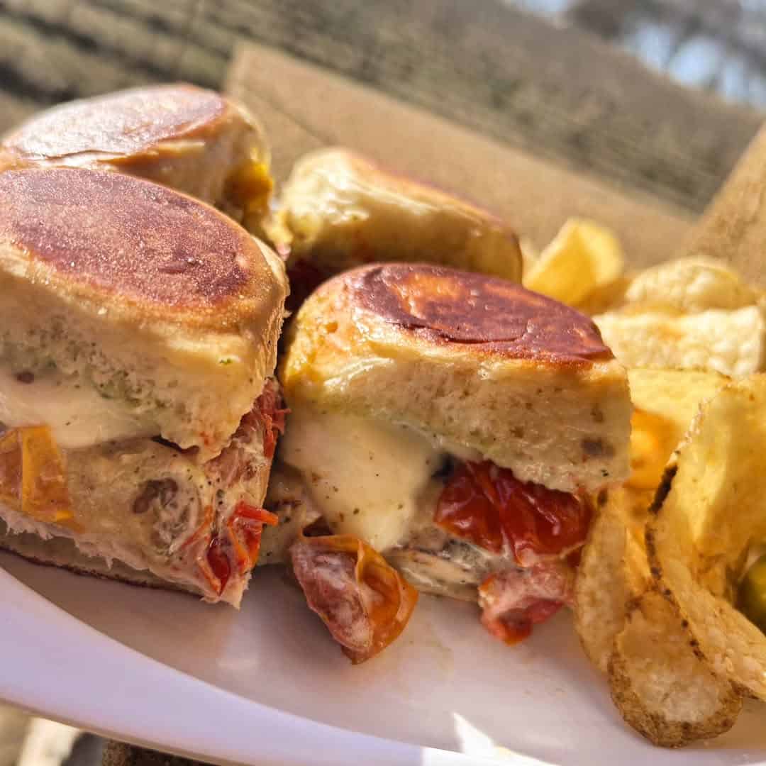 Close-up of toasted sandwiches with melted cheese and tomatoes, served with potato chips on a white plate&mdash;perfect for enjoying at finger lakes wineries with restaurants.