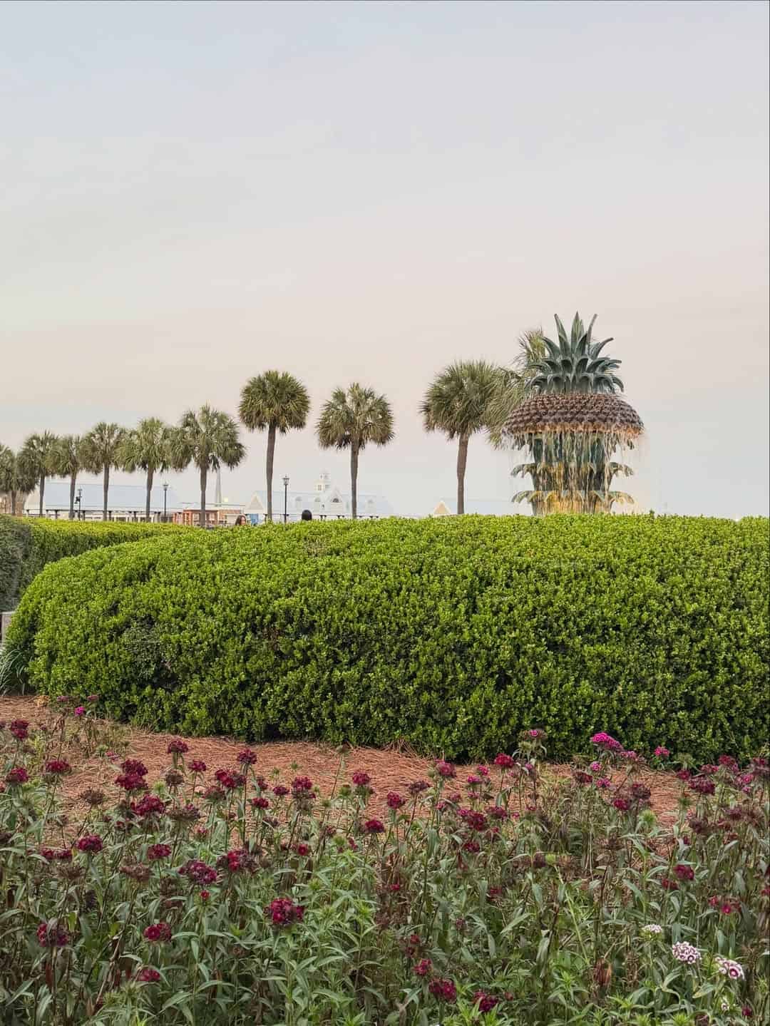 A large pineapple fountain with palm trees and flowers under a clear sky in a park setting—one of the top things to do in Charleston with kids.