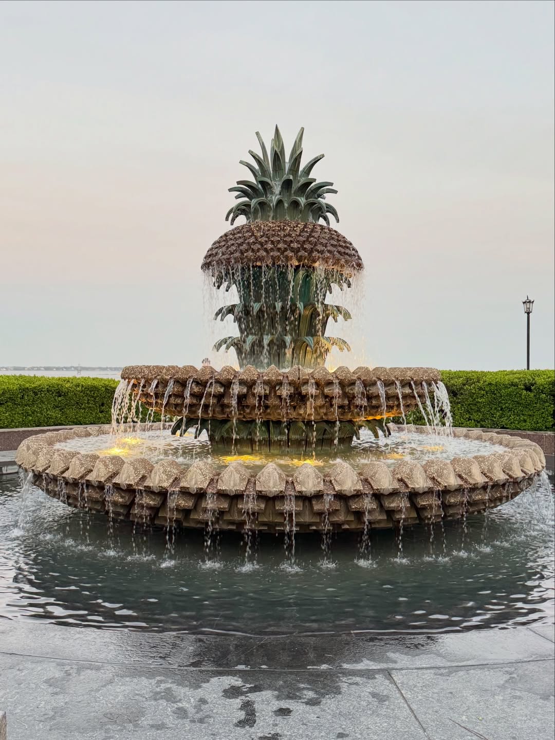 A large pineapple-shaped fountain with cascading water, surrounded by greenery and a cloudy sky—one of the top things to do in Charleston with kids for a fun family outing.
