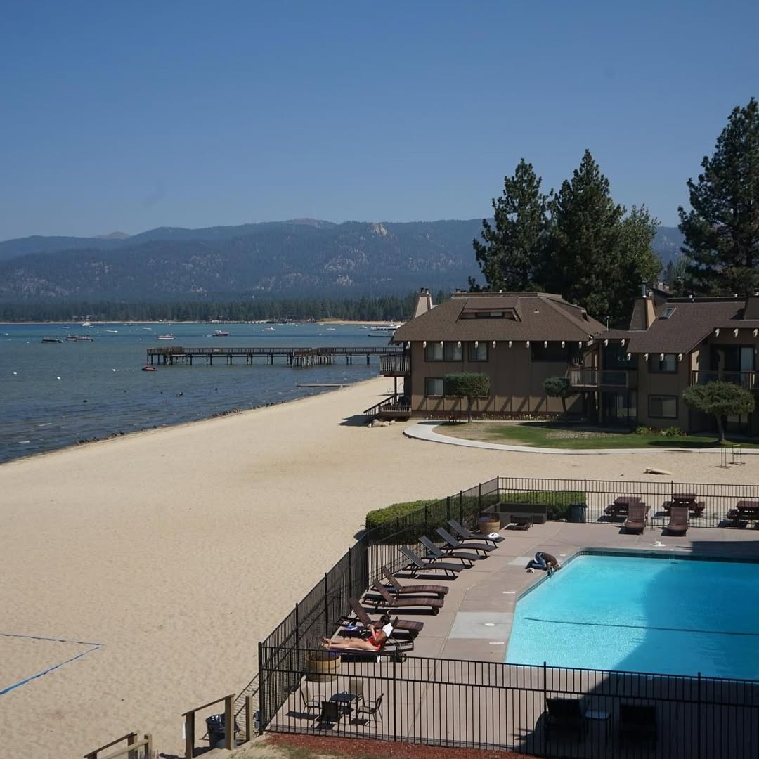 Beachfront resort with sandy shore, pool, lounge chairs, and mountains in the background under a clear sky—perfect for a relaxing family vacation to Lake Tahoe.