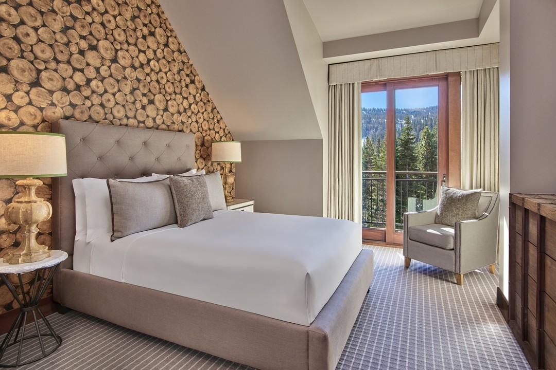 Cozy bedroom with wood accent wall, large window, bed, and armchair—perfect for a family vacation to Lake Tahoe, with beautiful views of trees and mountains outside.