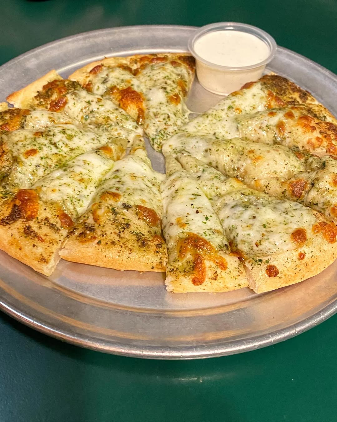 Cheesy garlic bread cut into slices on a metal plate with a cup of ranch dipping sauce—perfect for sharing after a family vacation to Lake Tahoe.