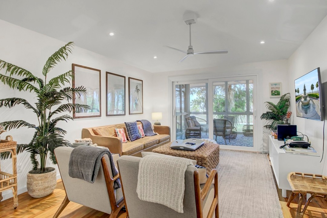 Bright living room with neutral furniture, tropical decor, indoor plants, and a view of a screened porch outside—perfect for planning things to do in Charleston with kids after a day of exploring.