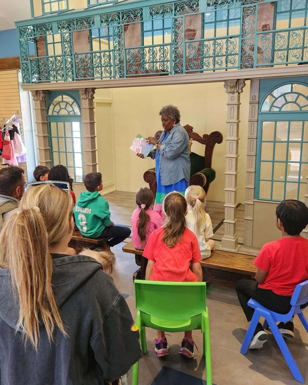 A woman reads a book to a group of children seated in front of her in a room with decorative blue arches—one of the delightful things to do in Charleston with kids.