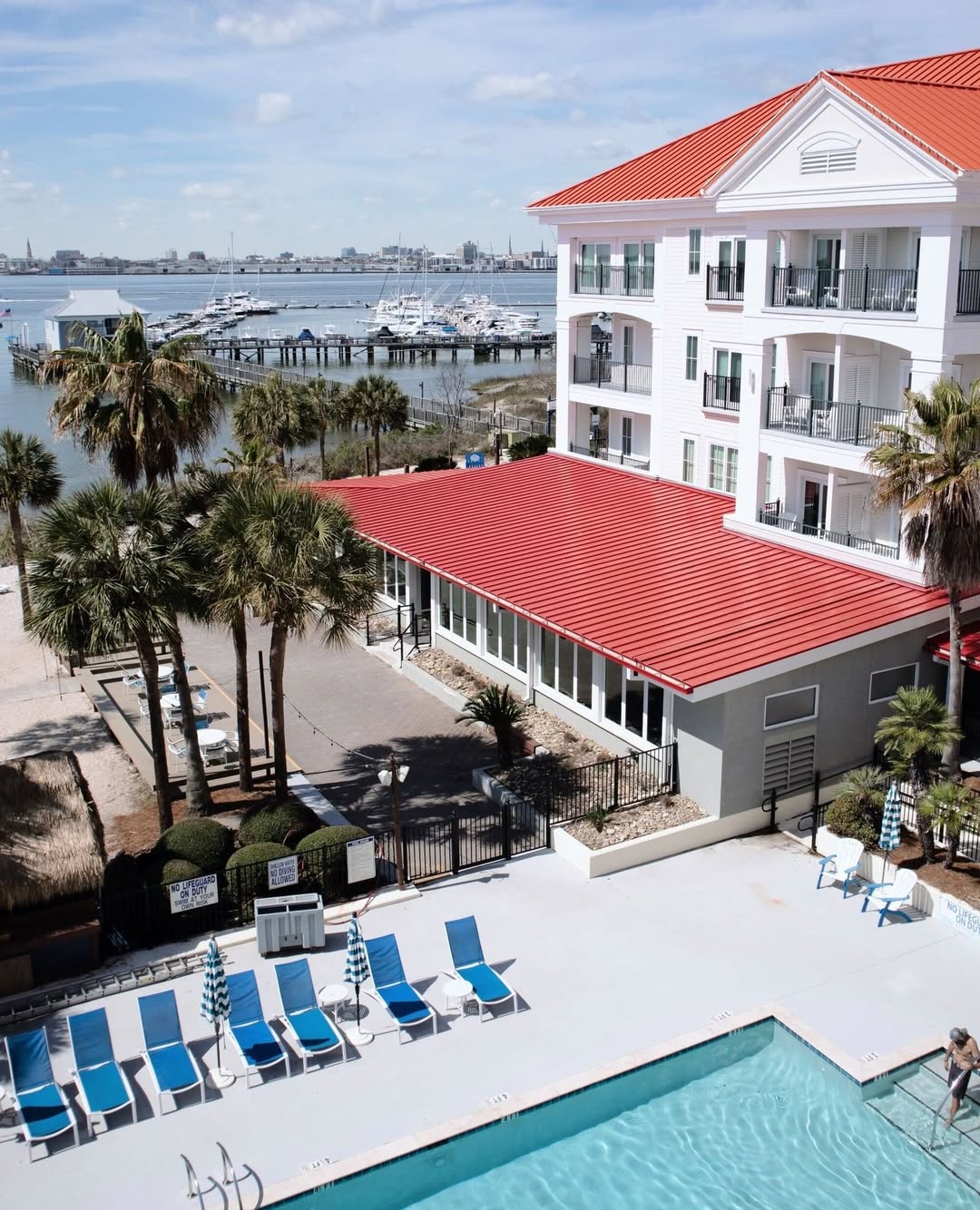 A hotel with a red roof overlooks a pool, palm trees, and a marina with boats on a sunny day—perfect for families seeking things to do in Charleston with kids.