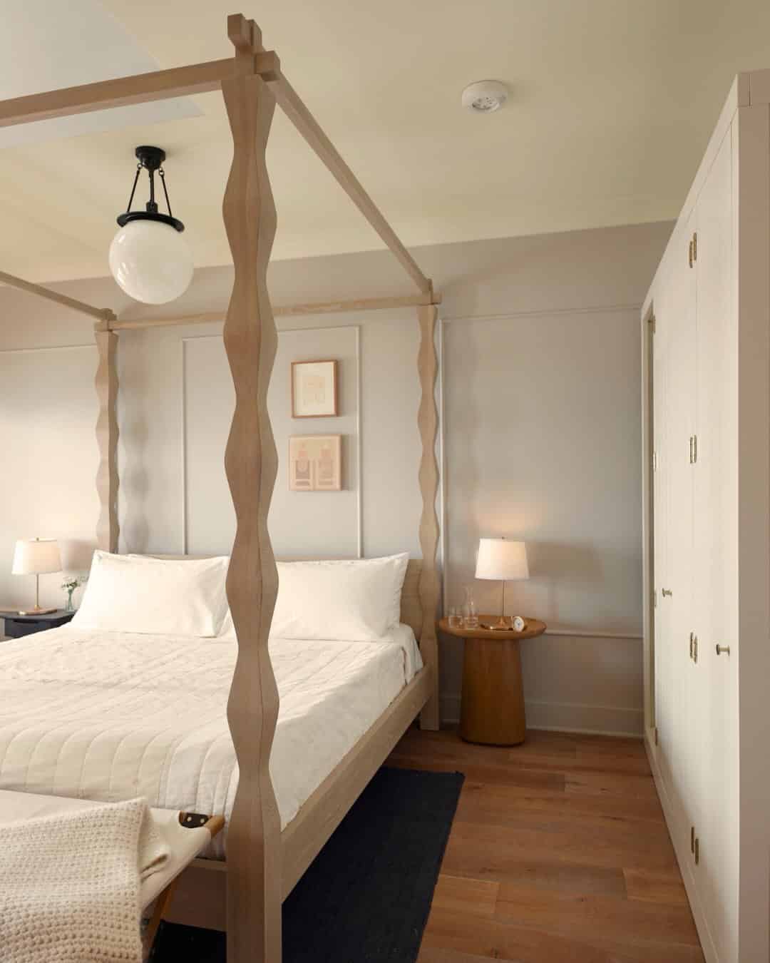 Modern bedroom with a wooden canopy bed, white bedding, nightstand, lamps, and framed art on the wall—perfect for those seeking the Best Places to Stay in Finger Lakes Near Wineries.