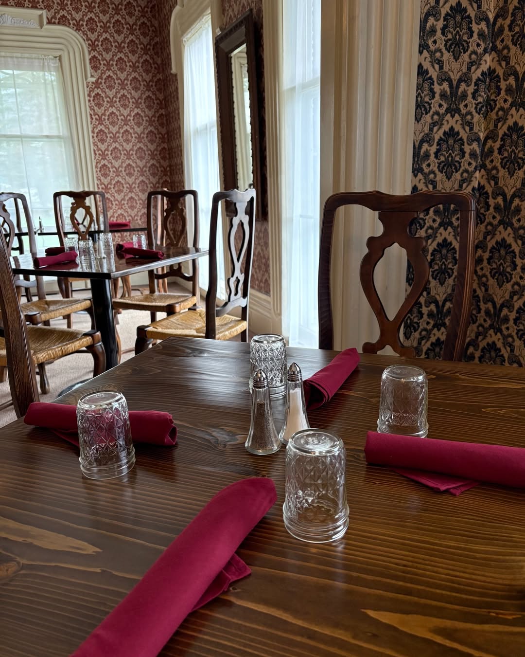 A wooden dining table set with red napkins, glasses, and silver shakers in a vintage-style restaurant—one of the charming scenes you’ll find at the Best Places to Stay in Finger Lakes Near Wineries.