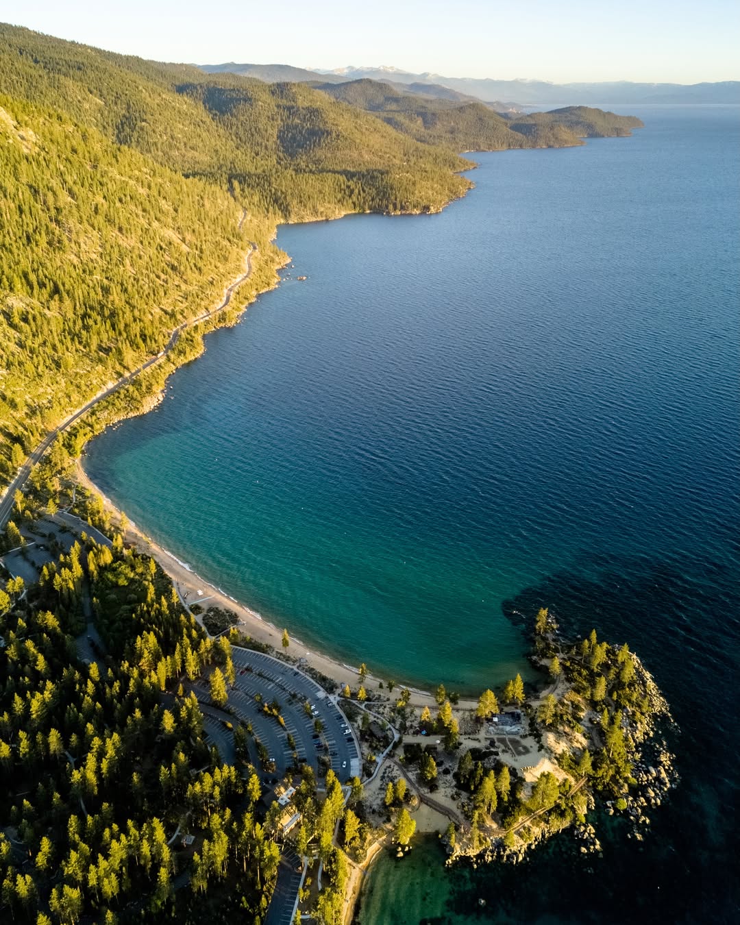 Aerial view of a winding coastline with a beach, forested hills, and clear blue water under sunlight—perfect inspiration for your next family vacation to Lake Tahoe.
