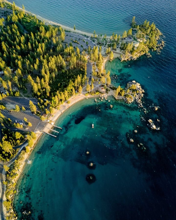 Aerial view of a forested coastline with clear blue water, small beach, and surrounding greenery—perfect for a relaxing family vacation to Lake Tahoe.