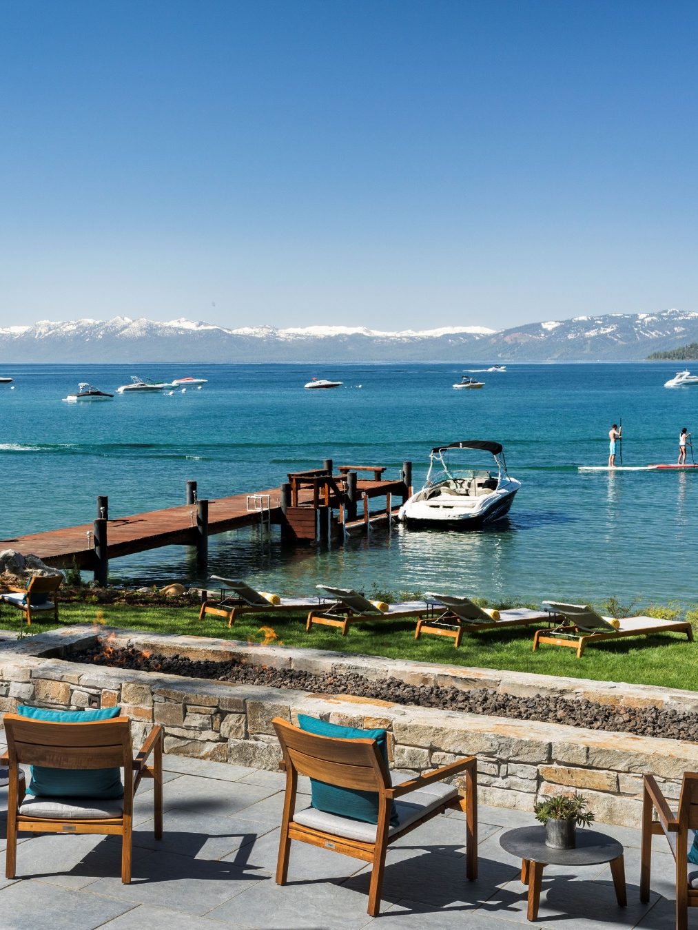 Lakeside patio with wooden chairs, a dock, boats on blue water, and mountains in the distance under clear skies—perfect for a family vacation to Lake Tahoe.