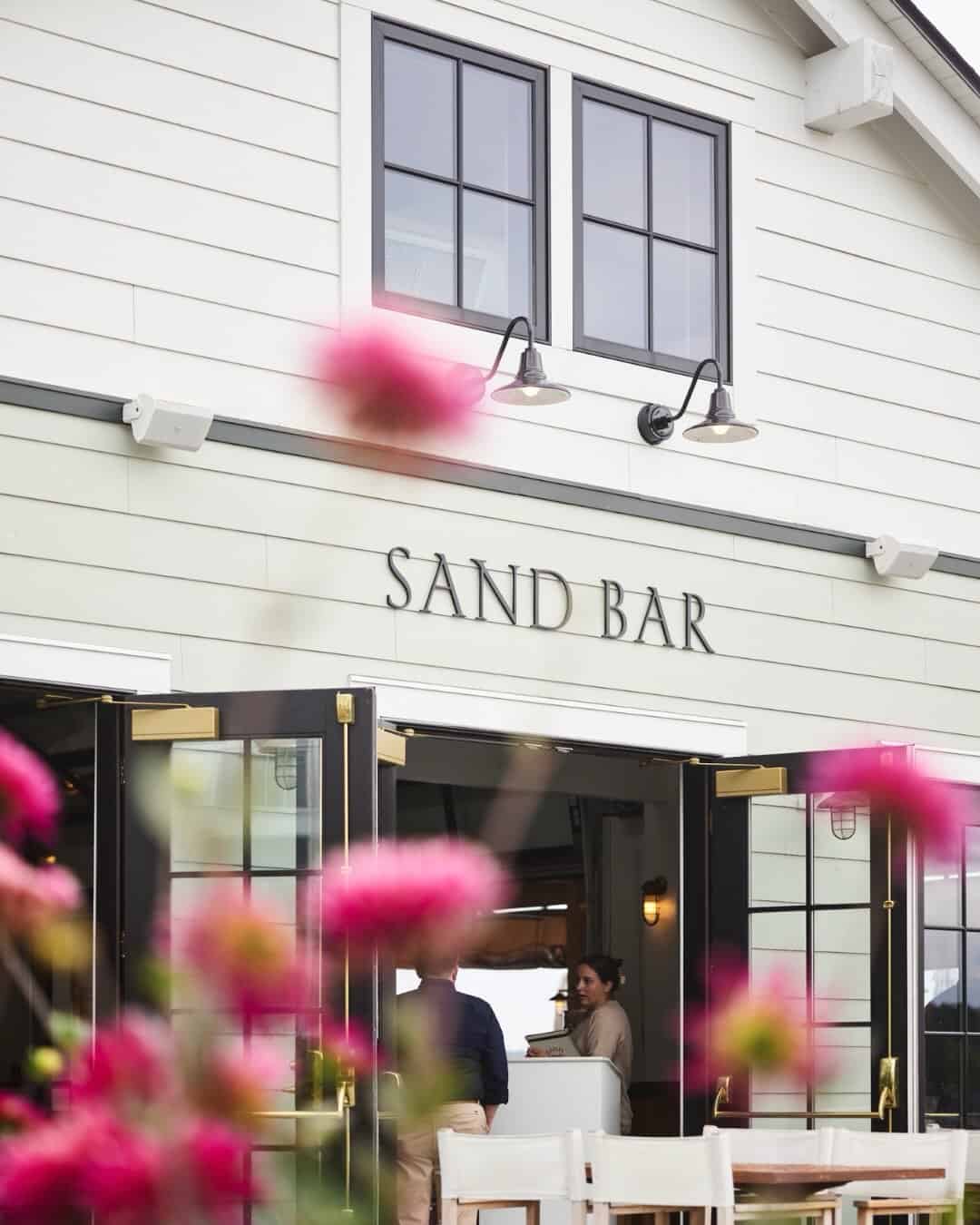 White building labeled "Sand Bar" with open doors and pink flowers in the foreground—one of the best places to stay in Finger Lakes near wineries.