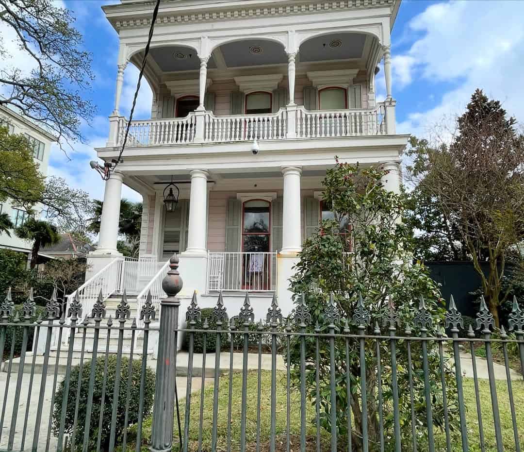 Victorian-style two-story house with columns, balconies, and an iron fence in front, surrounded by greenery—a classic spot to admire during your search for things to do in Charleston with kids.