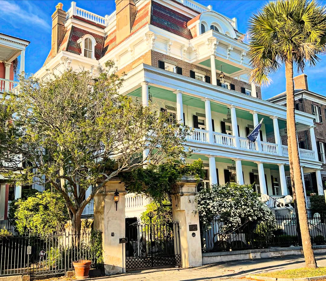 A large, historic three-story house with balconies, columns, trees, and a wrought iron gate in front—perfect for exploring when searching for things to do in Charleston with kids.