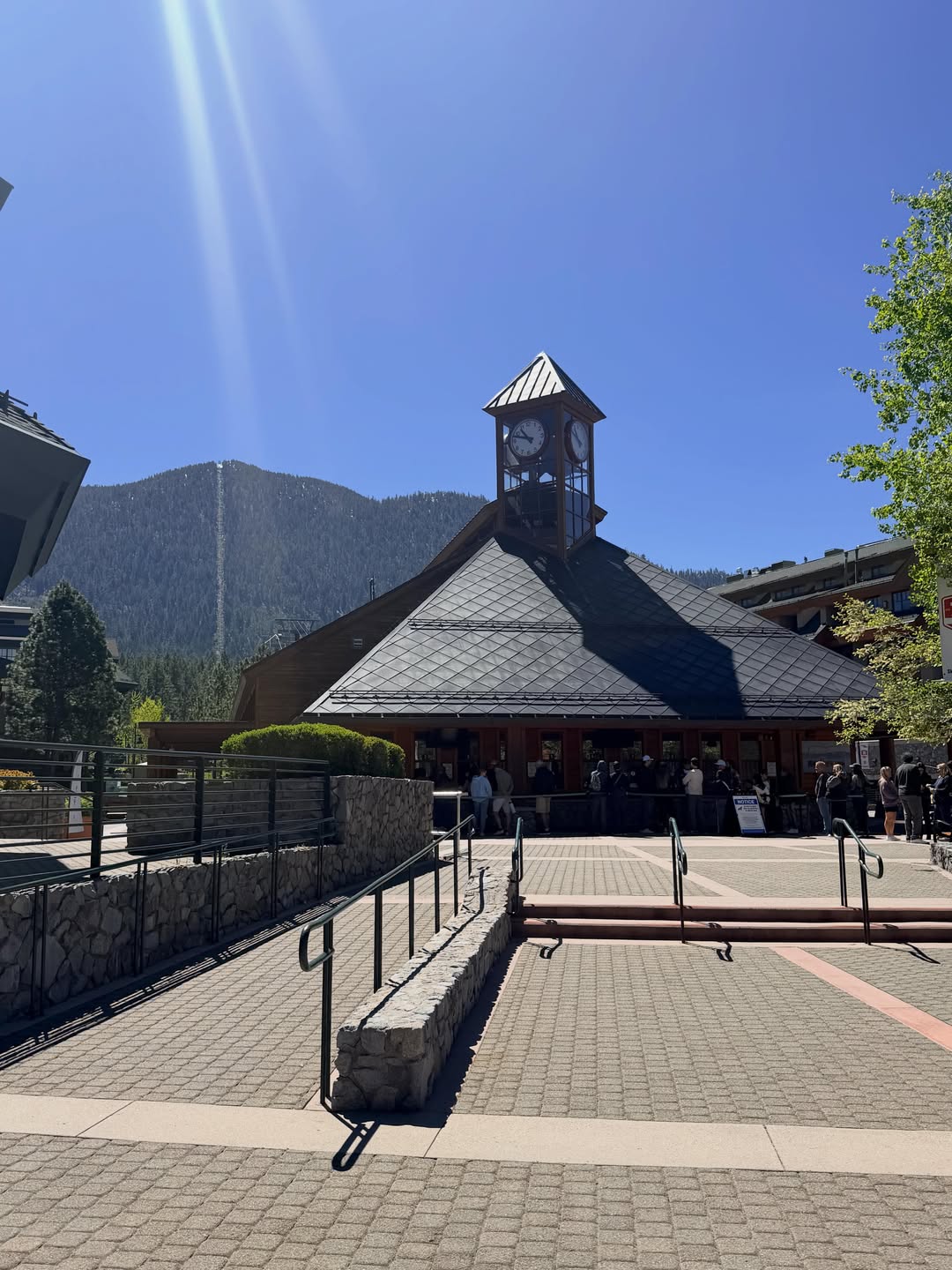 A clock tower building under a clear blue sky, with mountains and people gathered outside—perfect for capturing memories on a family vacation to Lake Tahoe.