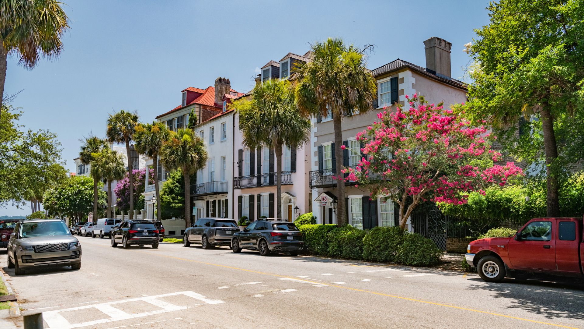 Colorful historic houses with balconies and palm trees line a sunny street with parked cars—perfect for exploring as one of the top things to do in Charleston with kids.