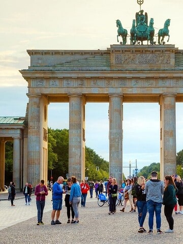 People gather in front of Berlin’s iconic Brandenburg Gate on a clear day.