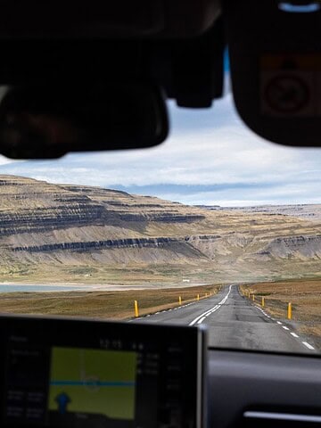 View from inside a car driving towards a flat-topped mountain, with hands on the steering wheel.