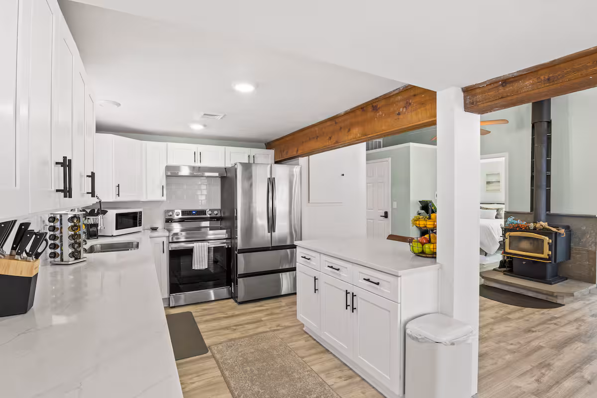 Modern kitchen with white cabinets, stainless steel appliances, and a view of a cozy living area with a wood stove—perfect for relaxing in one of the inviting Finger Lakes vacation rentals.