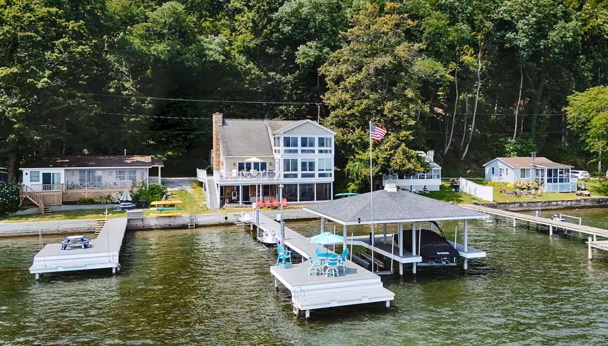 Lakeside cabins and cottages with docks and boats, surrounded by trees, and an American flag on one dock—perfect Finger Lakes vacation rentals.