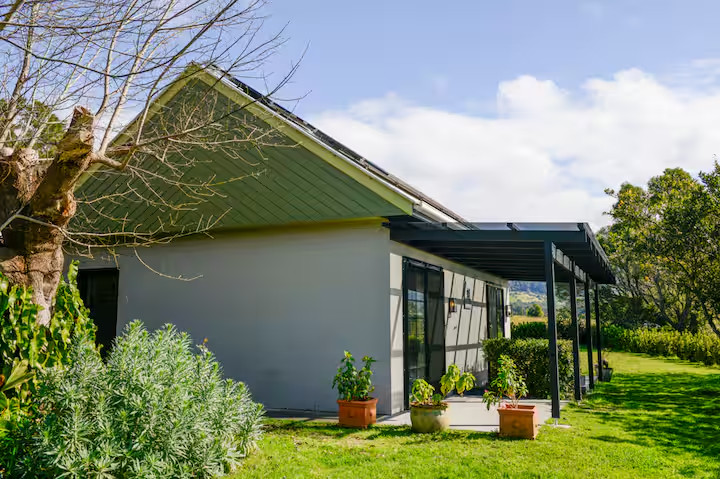A modern house with a green roof, patio, potted plants, and a grassy yard on a sunny day—perfect for those who love stylish cottages or are seeking unique Finger Lakes vacation rentals.