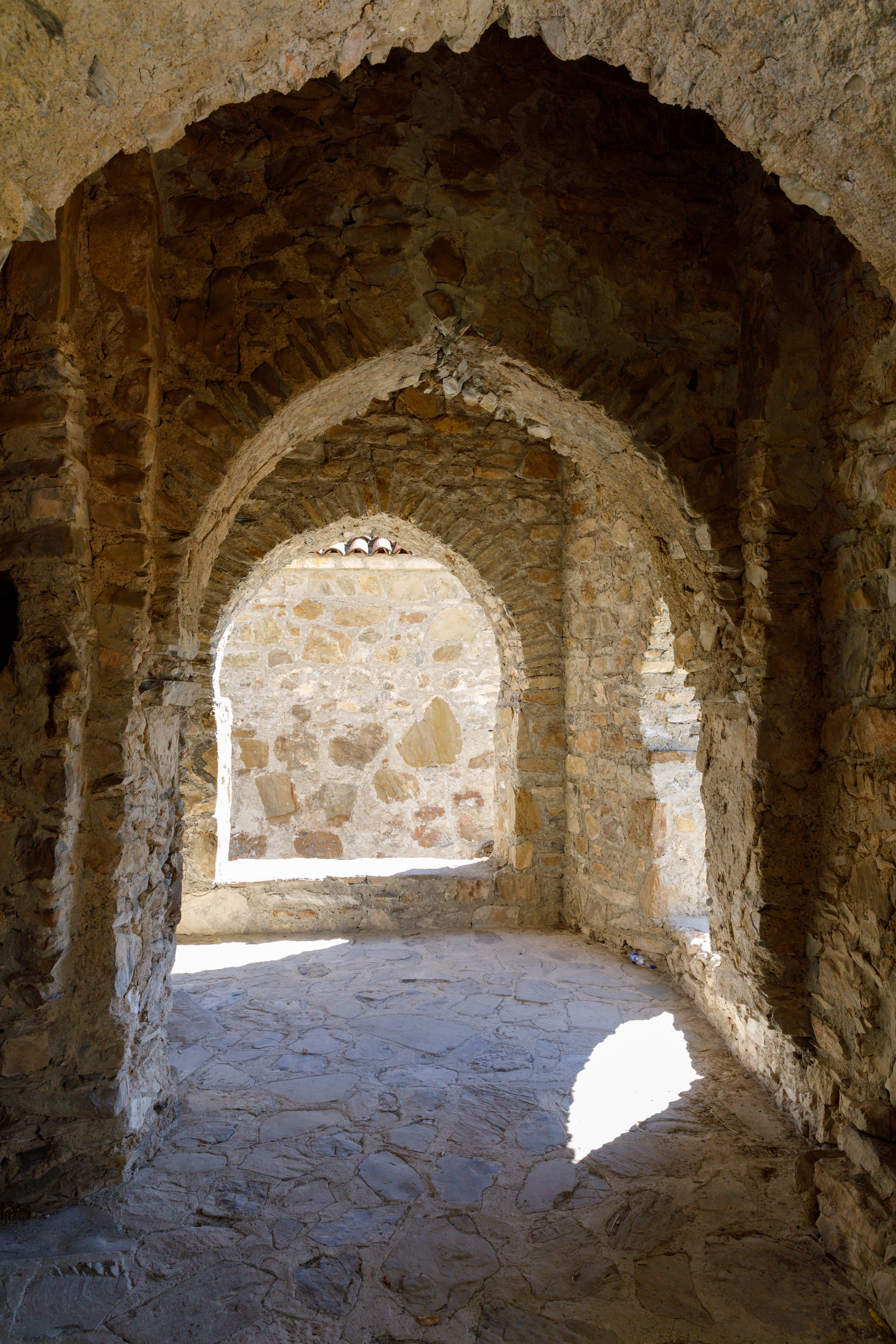 Stone archways and walls of an ancient ruin, sunlight casting shadows on the stone floor&mdash;an enchanting setting perfect for wine tourism enthusiasts to explore history while savoring local flavors.