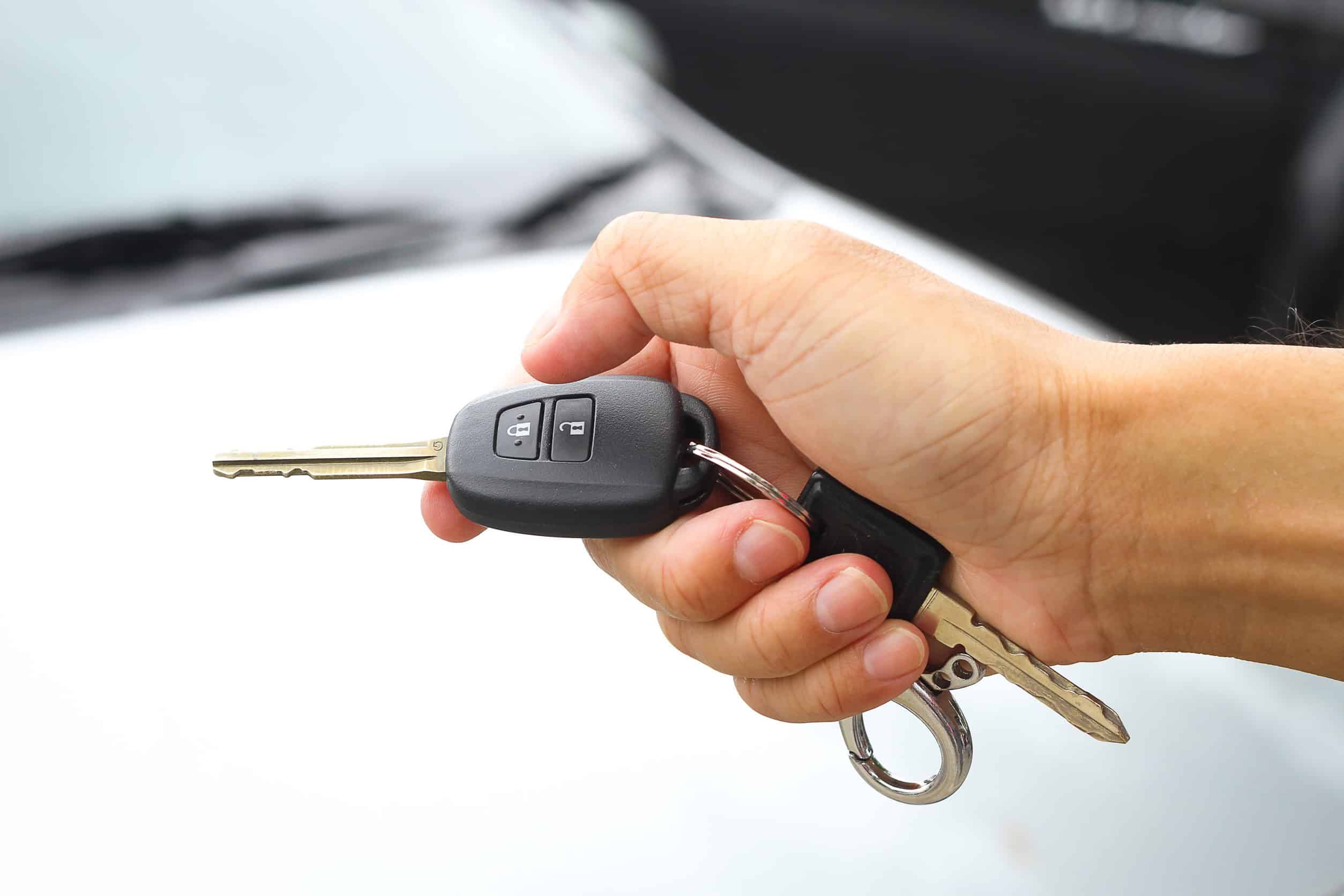 A hand holding a car key with a remote, with a white car in the background, capturing the essence of Grand Cayman luxury travel.